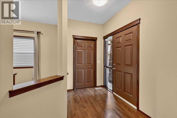 Interior view of a hallway with hardwood floors, a brown double door, and a dark brown entry door. - 277 Evermeadow Avenue Sw, Calgary