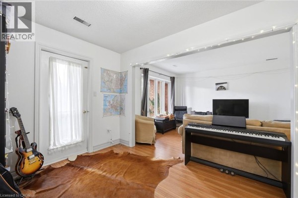 Living room with hardwood floors, a piano, couch, and a door leading outside. - 277 Harvie Avenue, York