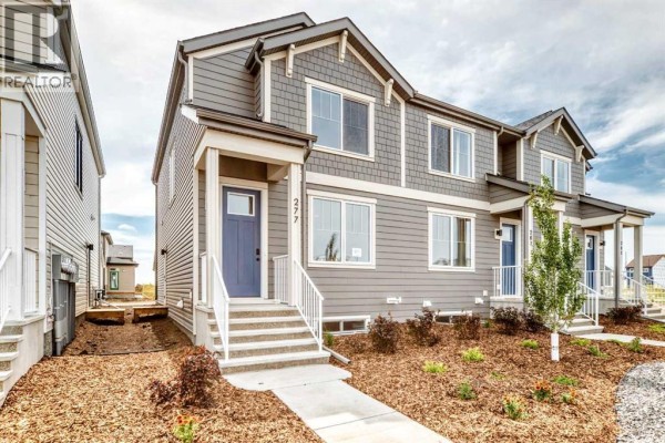 Front exterior of a grey townhouse with a blue front door and white trim, showing side yard. - 277 Heirloom Way Se, Calgary