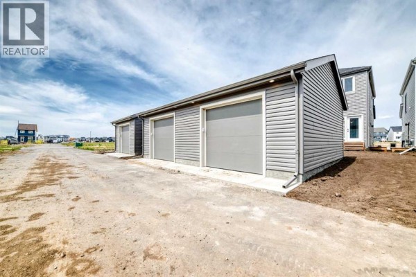 Rear exterior of a townhouse with a gravel driveway and three garage doors. - 277 Heirloom Way Se, Calgary
