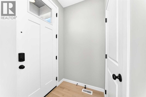 Interior entryway with a white door, light grey walls, and blonde wood laminate flooring. - 277 Heirloom Way Se, Calgary
