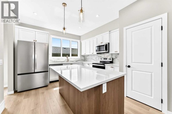 Modern kitchen with white cabinets, a large island, stainless steel appliances, and marble backsplash. - 277 Heirloom Way Se, Calgary