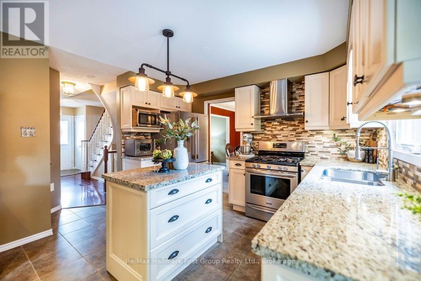 Kitchen with light wood cabinets, island, stainless steel range, and view of entryway stairs. - 278 St Joseph Road, Kawartha Lakes