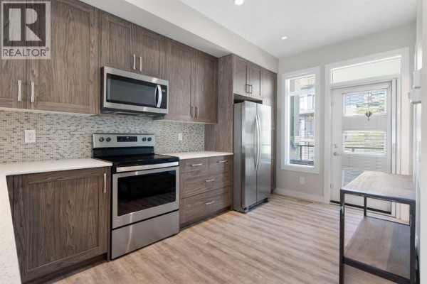 Kitchen with stainless steel appliances, grey wood cabinets, white countertops, and a mosaic tile backsplash. - 28, 138 Seton Passage Se, Calgary