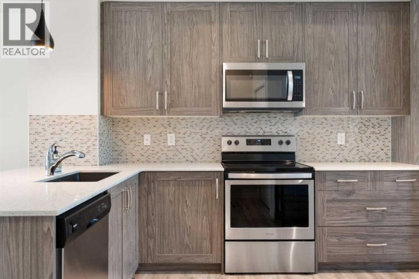 Another view of the kitchen featuring grey wood cabinetry, white quartz countertops, and stainless steel appliances. - 28, 138 Seton Passage Se, Calgary