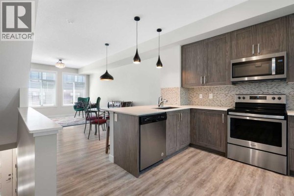 Open concept kitchen and dining area with light wood floors, modern pendant lights, and large windows. - 28, 138 Seton Passage Se, Calgary