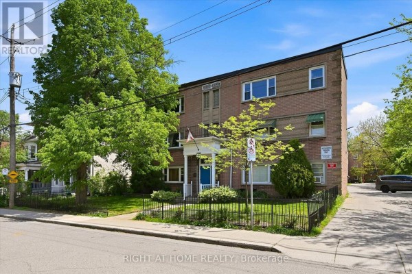 Side view of the brick apartment building with green lawn and black fence. - 28 - 137 Emerald Street S, Hamilton