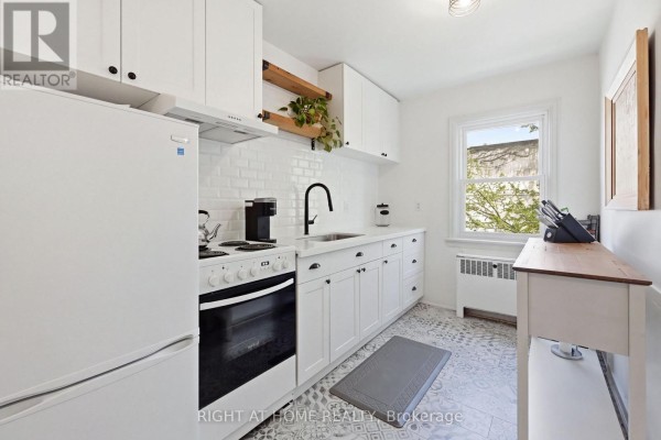 White kitchen with subway tile backsplash, white cabinets, and hardwood flooring. - 28 - 137 Emerald Street S, Hamilton