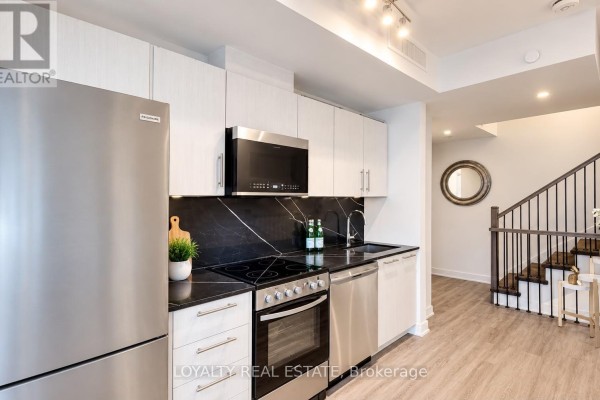 Modern kitchen with white cabinets, black backsplash, stainless steel appliances, and stairs. - 28 - 861 Sheppard Avenue W, Toronto