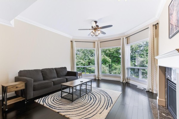 Living room with dark hardwood floors, grey sofa, coffee table, and bay windows. - 28 32777 Chilcotin Drive, Abbotsford