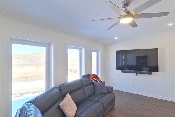 Living room with black leather sofa, large television, ceiling fan, and wide windows overlooking a field. - 28-590059 Range Road 110, Rural Woodlands County