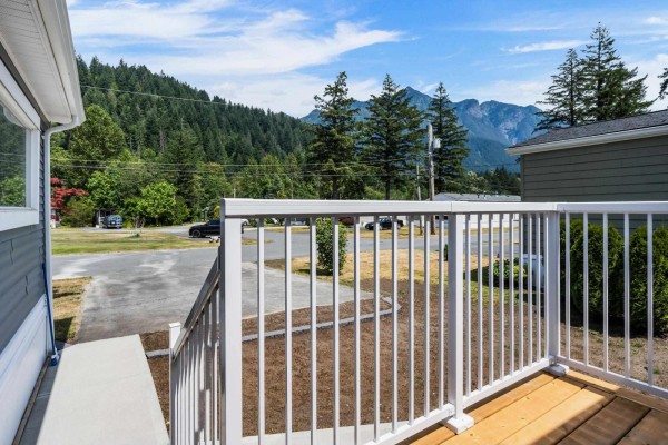 View from a wooden deck with white railings overlooking a paved road, trees, and mountains. - 28 65367 Kawkawa Lake Road, Hope, Hope
