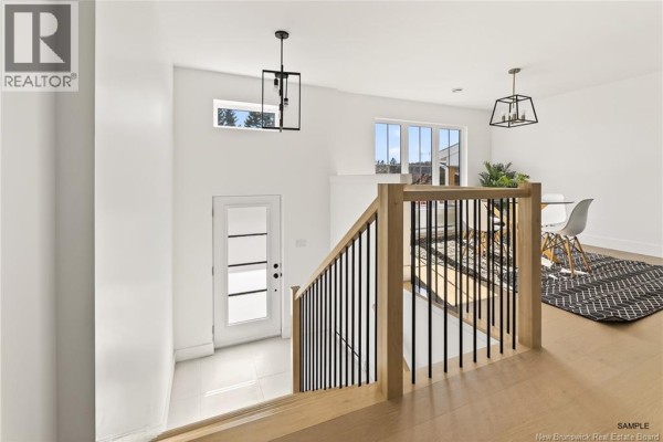 Bright room with large window, modern light fixture, and hardwood flooring, adjacent to kitchen area. - 28 Adéo-rose Street, Memramcook