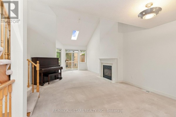 Living room with a fireplace, piano, vaulted ceiling, and a skylight. - 28 Blue Heron Beach Way, Markham