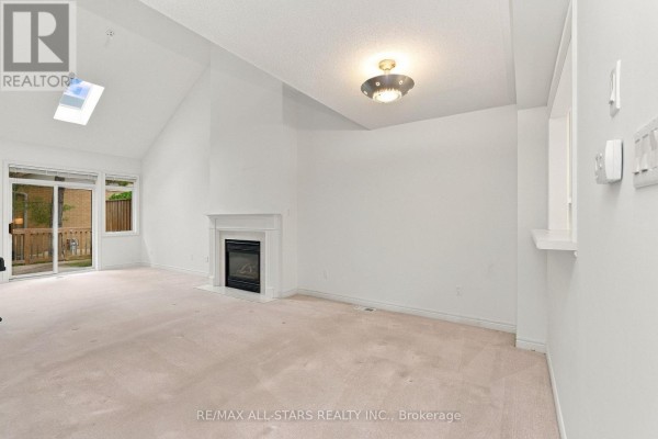 Living room with a fireplace, vaulted ceiling, skylight, and a view of the backyard. - 28 Blue Heron Beach Way, Markham