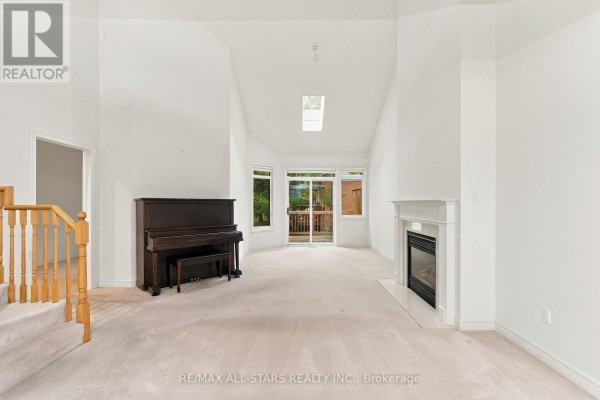 Living room with a piano, fireplace, vaulted ceiling, skylight, and sliding glass doors. - 28 Blue Heron Beach Way, Markham
