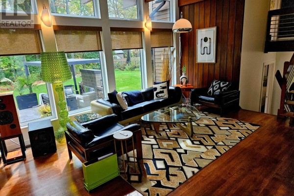 Living room with floor-to-ceiling windows, dark leather furniture, and a patterned area rug on wood floors. - 28 Burnbank Street, Ottawa