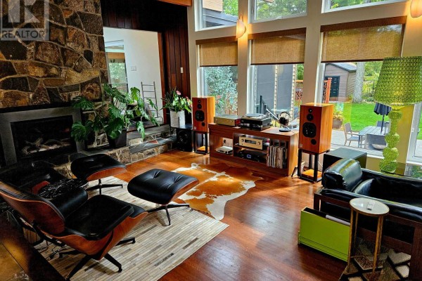 Living room with a stone fireplace, Eames lounge chairs, a stereo system, and large windows. - 28 Burnbank Street, Ottawa