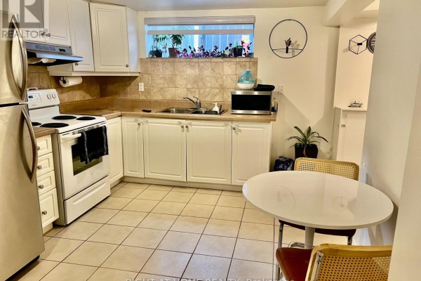 Kitchen with white cabinetry, beige tiled backsplash, white appliances, and a small dining table with two chairs. - 28 Gorman Park Road, Toronto