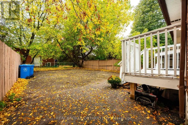 Backyard with a wooden deck, gravel ground covered in leaves, and a blue bin. - 28 Hillside Drive, Orangeville