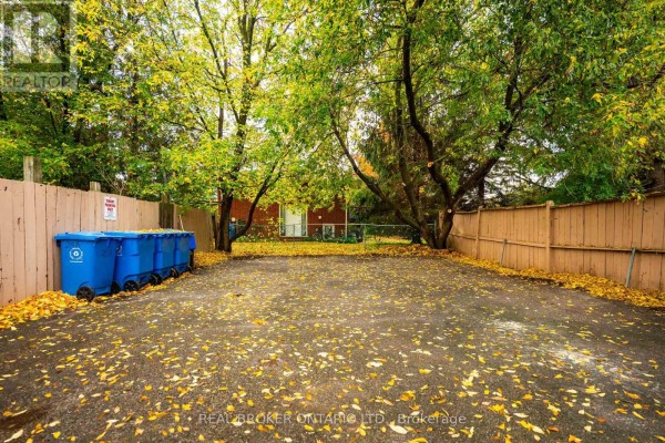 Rear view of the property with a gravel lot, multiple blue bins, and wooden fencing. - 28 Hillside Drive, Orangeville