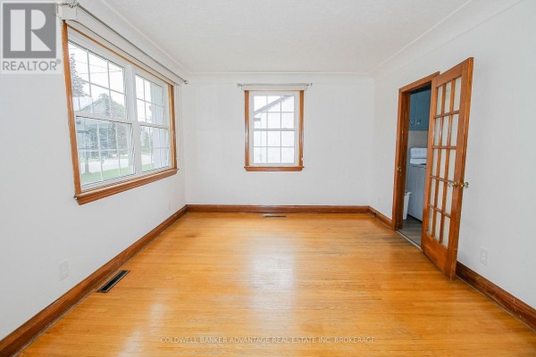 Hardwood floors and two windows in living room with laundry area access - 28 Marshall Avenue Welland