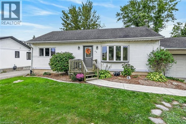 Front entrance of a white bungalow with a wooden porch and landscaped garden beds. - 28 Nelles Street E, York