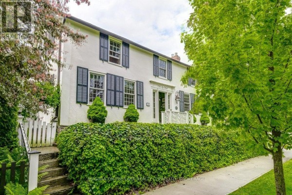 Side view of a white home with black shutters and ivy-covered landscaping, showing stairs and a fence. - 28 Prideaux Street, Niagara On The Lake