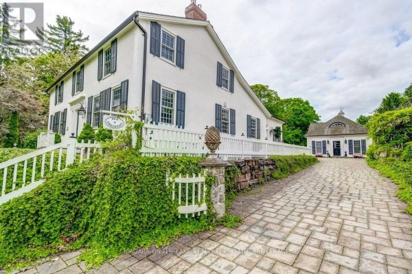 A white house with a stone gatepost, white picket fence, and a cobblestone driveway leading to a garage. - 28 Prideaux Street, Niagara On The Lake