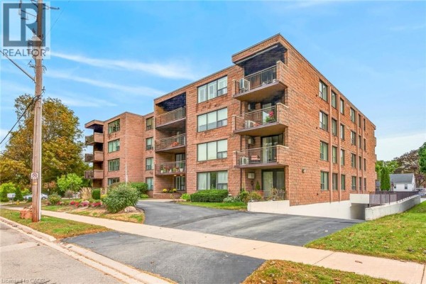 Side view of a brick apartment building with balconies and paved parking area. - 28 Robinson Street N Unit# 103, Grimsby