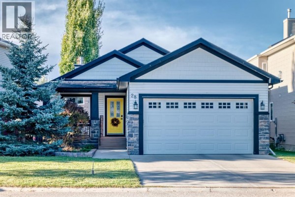 Front exterior of a beige house with a yellow door and a double garage. - 28 Sheep River Cove, Okotoks