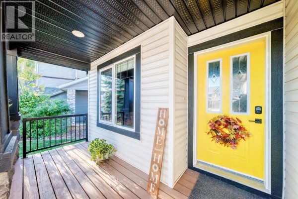 Covered front porch with a yellow door, flanked by windows and a "HOME" sign. - 28 Sheep River Cove, Okotoks