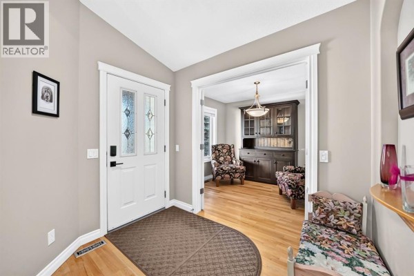 Entrance foyer with a white door, leading to a living area with floral chairs and a hutch. - 28 Sheep River Cove, Okotoks