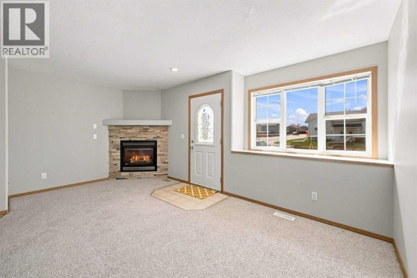 Living room of townhouse unit 28, featuring a gas fireplace, grey carpet, and large window. - 28 Terrace Heights Drive, Lacombe