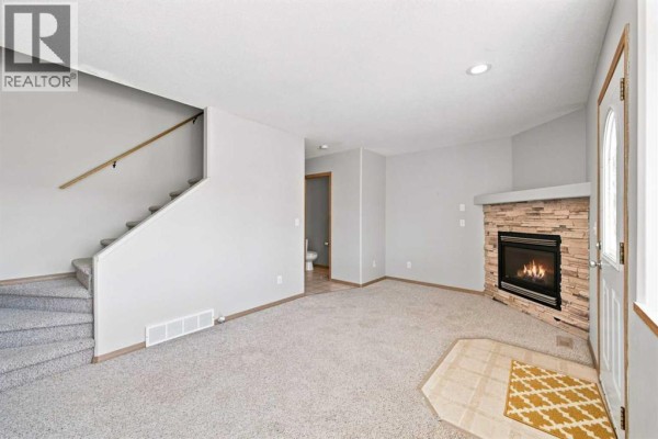 Living room with view of staircase, fireplace, and entrance of townhouse unit 28. - 28 Terrace Heights Drive, Lacombe