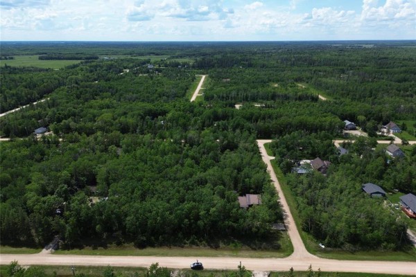 Aerial view of a rural area with many wooded lots, some with houses, and unpaved roads under a partly cloudy sky. - 28 Twin Pine Road, Gimli Rm