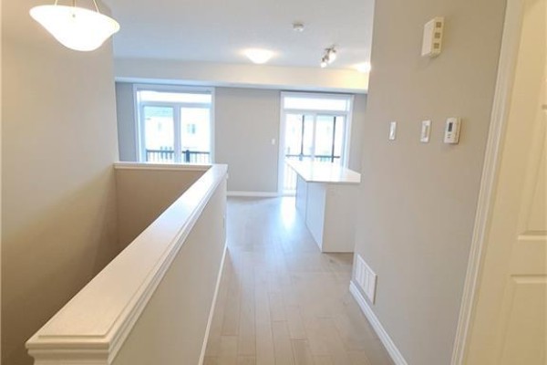 View from hallway overlooking open concept living area with kitchen island and balcony door. - 28 Wheat Lane, Kitchener