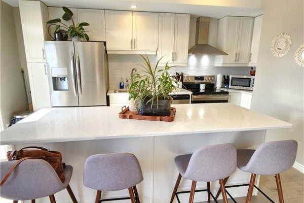 Kitchen island with grey stools and white quartz countertop facing stainless steel appliances. - 28 Wheat Lane, Kitchener