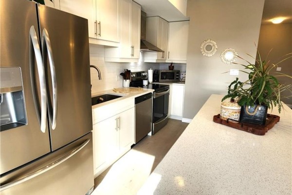 Kitchen with white cabinetry, stainless steel appliances, and quartz countertop island with stools. - 28 Wheat Lane, Kitchener
