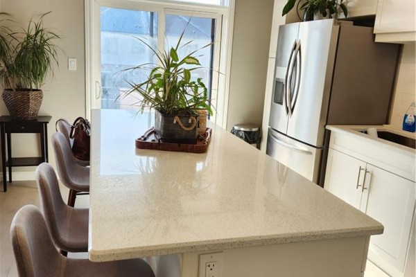 Kitchen island with stools facing stainless steel refrigerator and white cabinetry with sink. - 28 Wheat Lane, Kitchener
