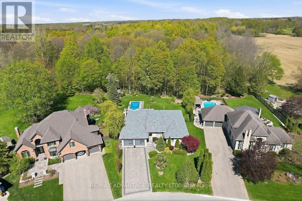 In-ground swimming pool surrounded by stone patio and lush greenery. - 28 Wynfield Lane, Middlesex Centre
