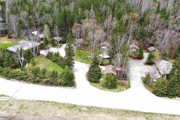 Aerial view of multiple small cabins and buildings clustered among dense trees and winding asphalt driveways. - 280 Highway 17, Wawa