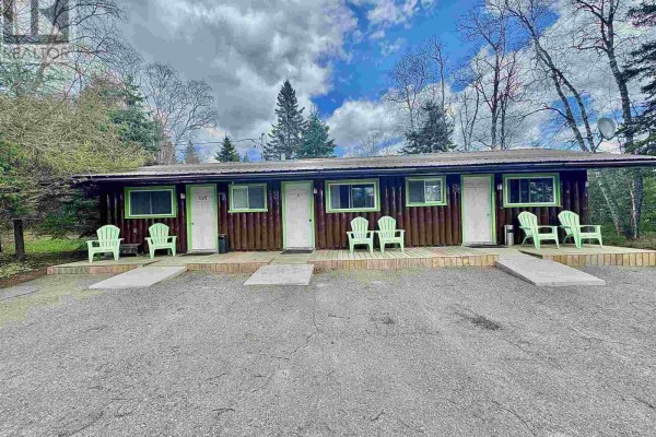 Exterior of a long, low log building with six numbered doors, each with a green frame and light green chairs. - 280 Highway 17, Wawa