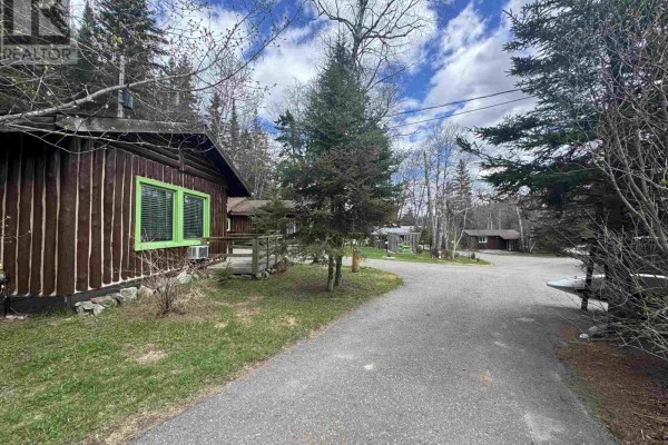 View of a log cabin with green trim windows, with a paved path leading further into a wooded area with cabins. - 280 Highway 17, Wawa