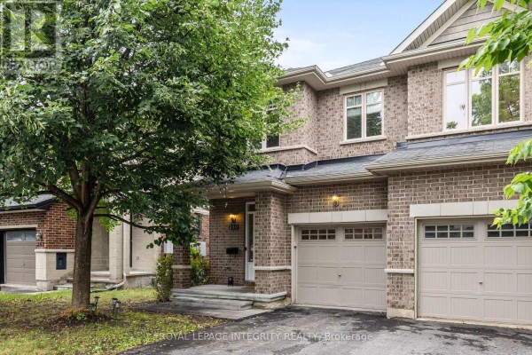 Close-up exterior view of a brick townhouse with light beige siding accents and two garage doors. - 280 Keyrock Drive, Ottawa