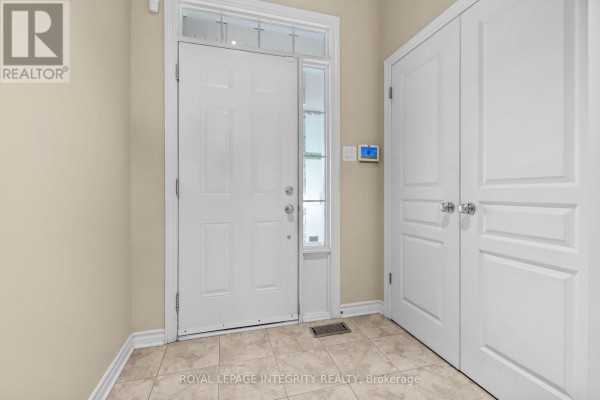 Interior view of a townhouse entrance with a white door, beige walls, tiled floor, and a double closet. - 280 Keyrock Drive, Ottawa