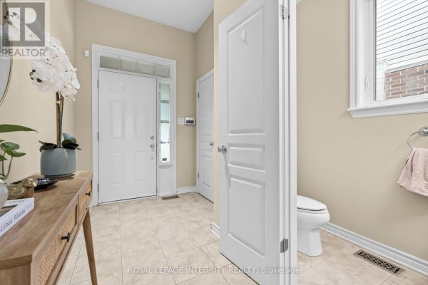 Interior view of a townhouse entrance area with a white door, beige walls, tiled floor, and a powder room. - 280 Keyrock Drive, Ottawa