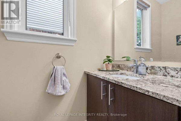 Powder room in a townhouse with a granite vanity, dark wood cabinets, toilet, and a towel ring. - 280 Keyrock Drive, Ottawa