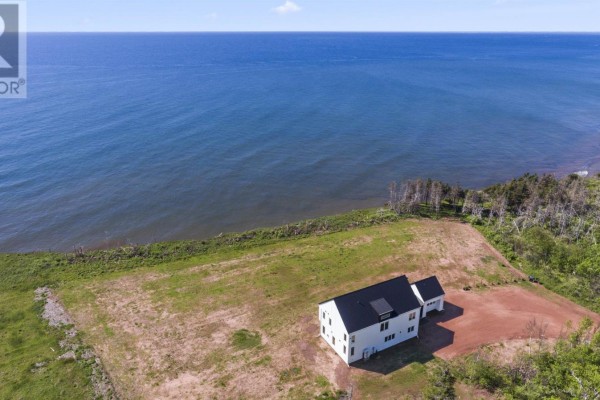 Aerial view of white house with black roof situated on grassy lot near ocean. - 280 Lighthouse Road, East Point