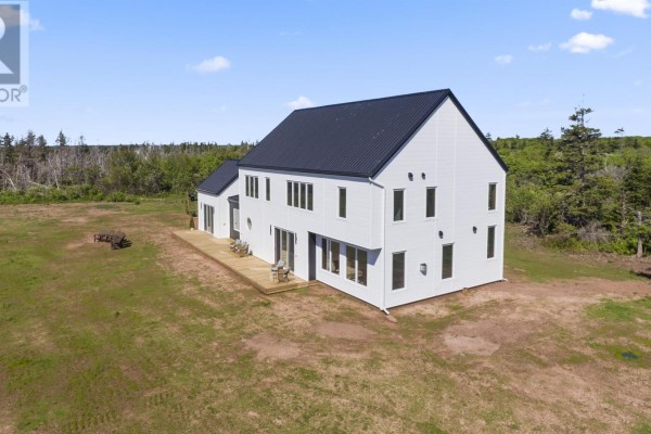 Rear exterior of white house with black roof and wooden deck in grassy field. - 280 Lighthouse Road, East Point